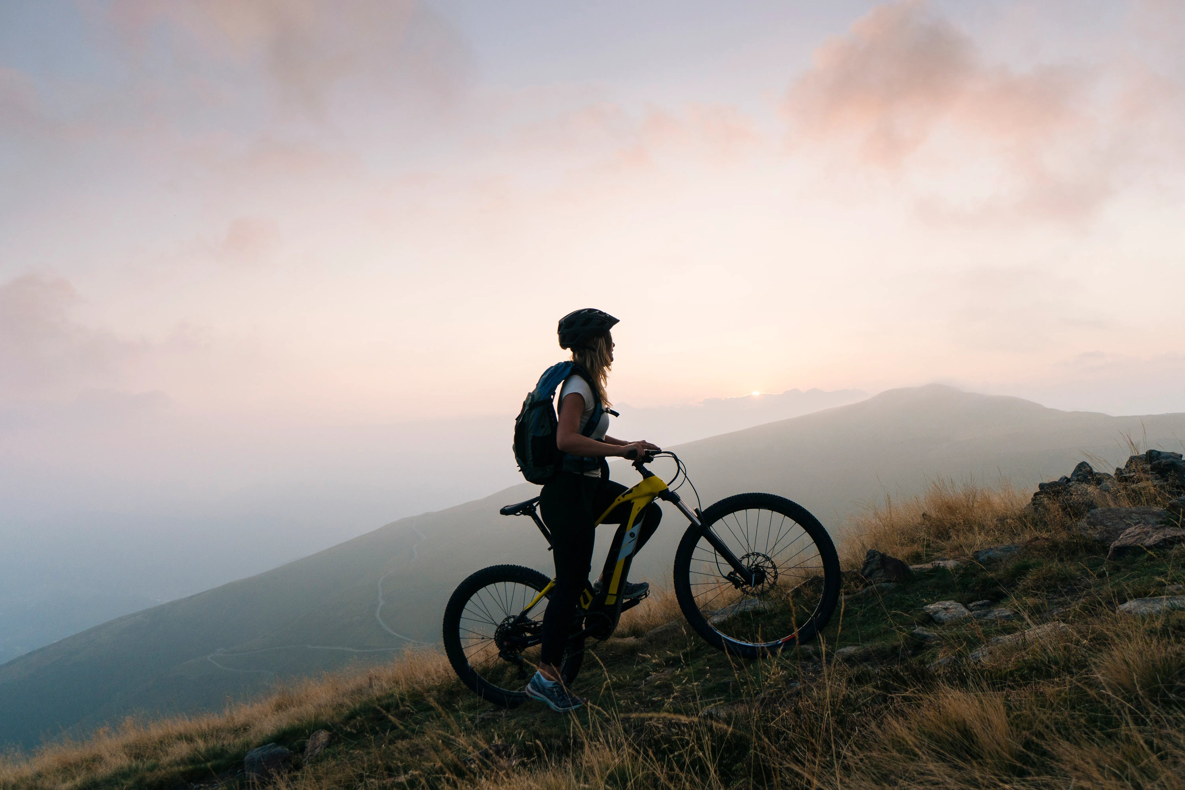 Person with a bicycle standing on a mountain top at sunset