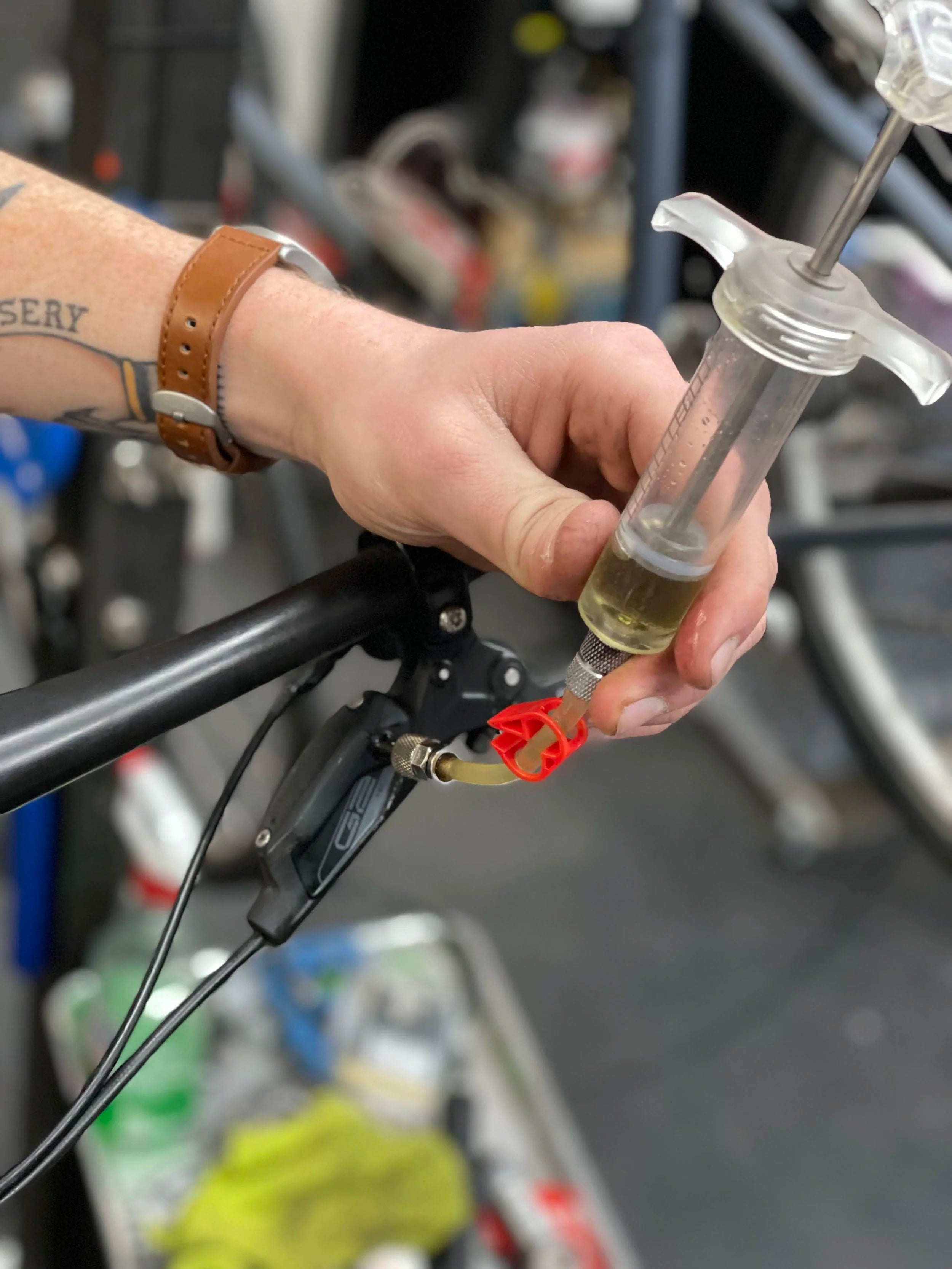 Person adjusting a bicycle's brake lever with a syringe-like tool.