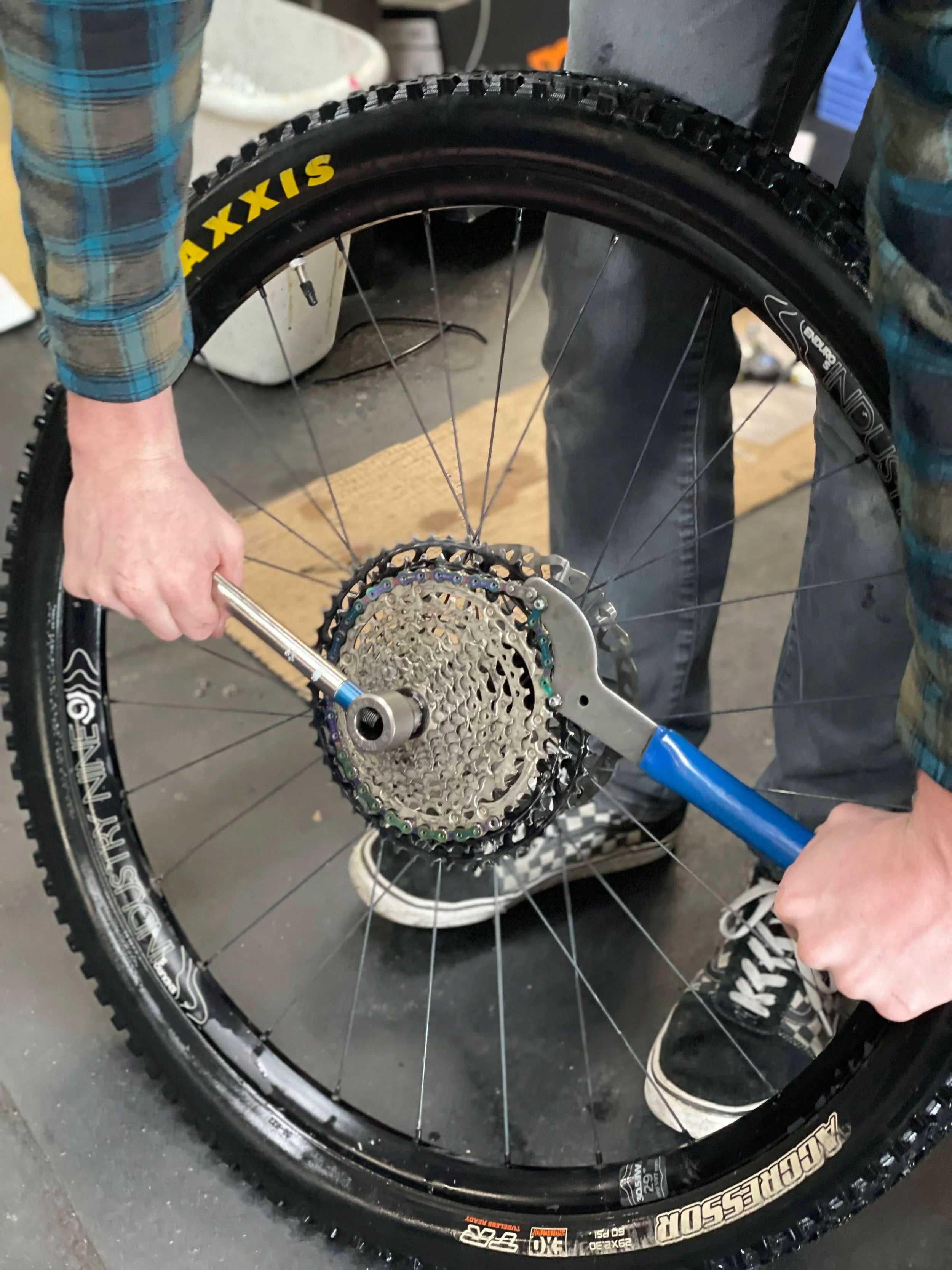 Person changing a bicycle tire with a tool on a concrete floor.